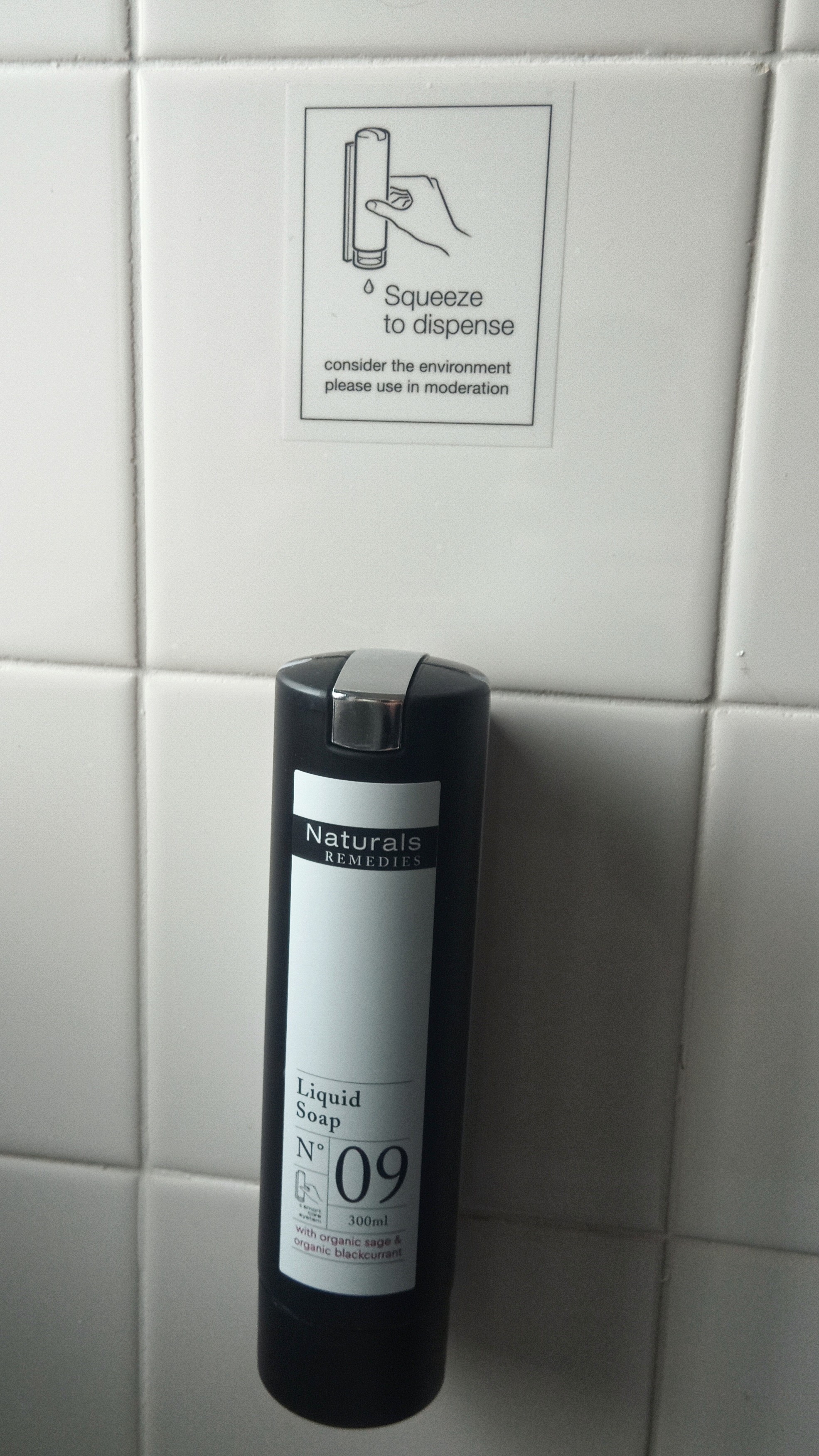 cylinder-shaped liquid hand soap dispenser with sign above saying "squeeze to disperse".